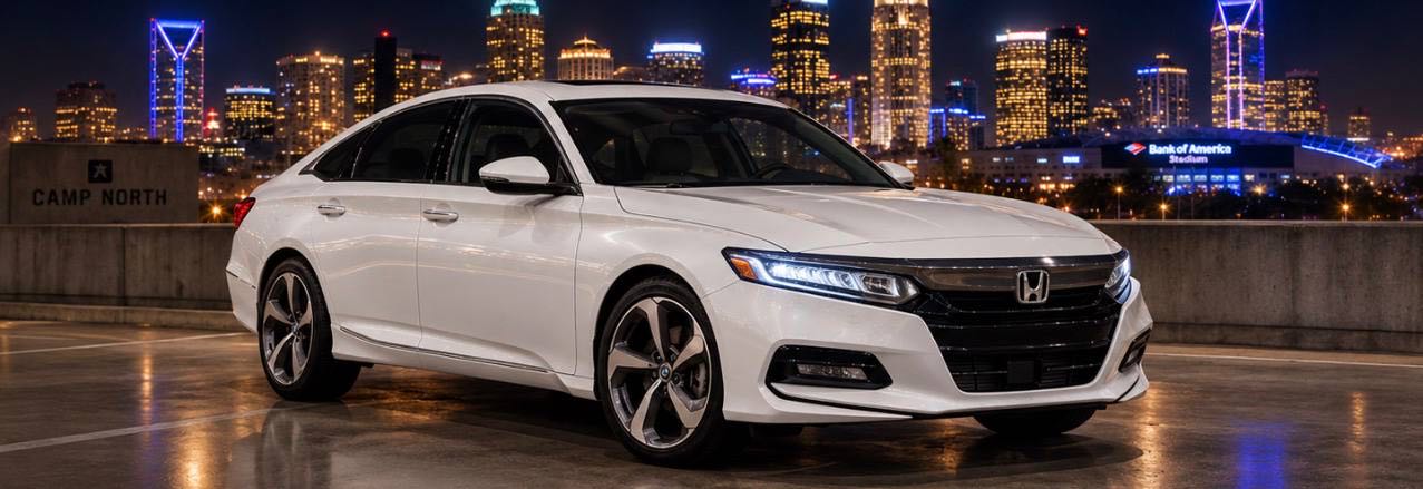 White Honda Accord sedan on a rooftop parking deck with the Charlotte skyline at night