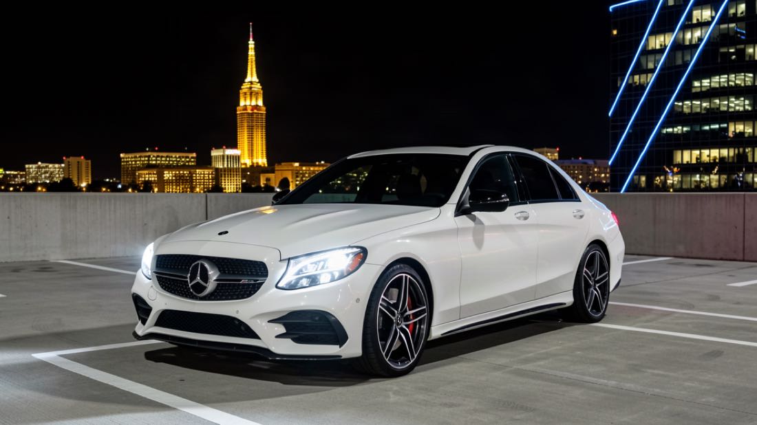 White 2017 Mercedes-Benz C300 sedan on a rooftop parking deck with the Charlotte skyline at night